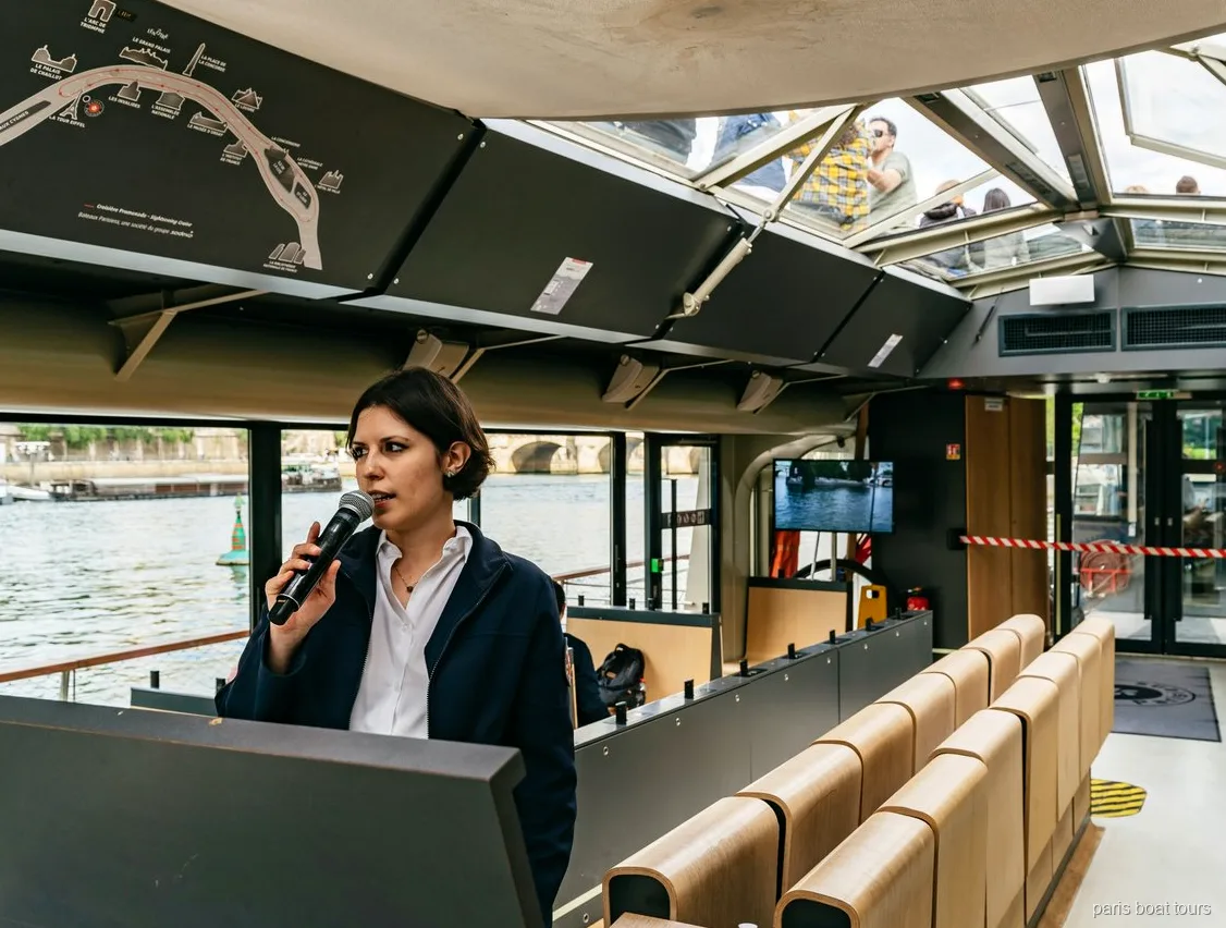 Guide avec un micro dans un bateau à toit vitré près d'une carte du parcours, croisières à Paris