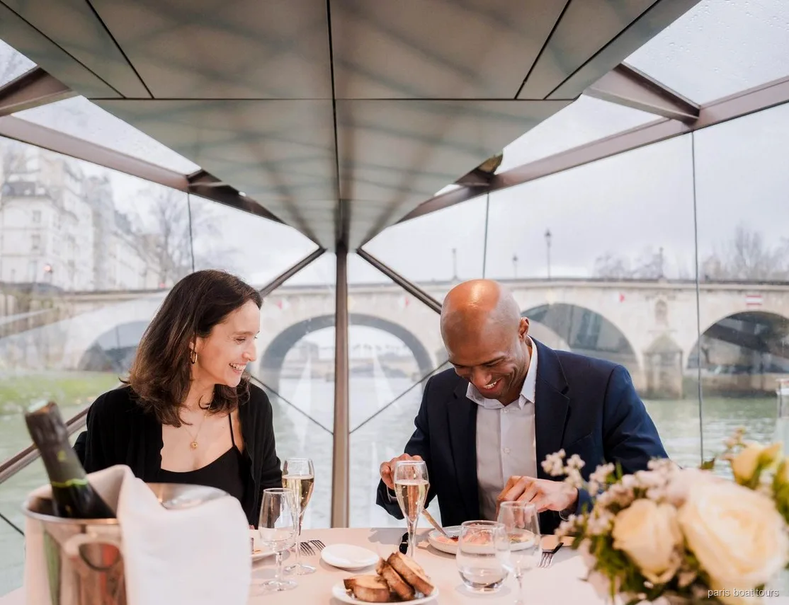 Stel glimlacht tijdens het diner met champagneglazen onder een glazen dak, brug buiten, boottochten in Parijs