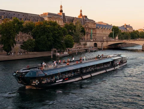 Bateaux Mouches boat gliding along the Seine at dusk past historic stone buildings on Paris boat tours