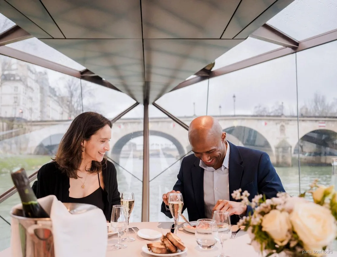 Paar lächelt beim Abendessen mit Champagnergläsern unter einem Glasdach, Brücke draußen, Paris Bootstouren