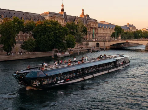 Bateaux Mouches-båd sejler på Seinen i skumringen forbi historiske stenbygninger på en sejltur i Paris