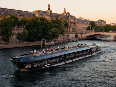 Bateaux Mouches-båt glider fram på Seine i skymningen förbi historiska stenbyggnader, båtturer i Paris