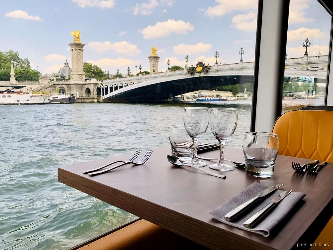 Zastawiony stolik przy oknie na rejsie paris boat tours z widokiem na most Aleksandra III nad Sekwaną