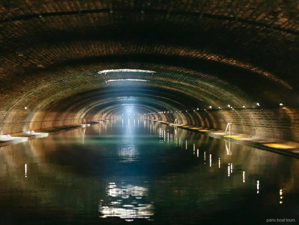 Gewölbter Backsteintunnel mit Lichtstrahl über dem Wasser auf Bootstouren in Paris