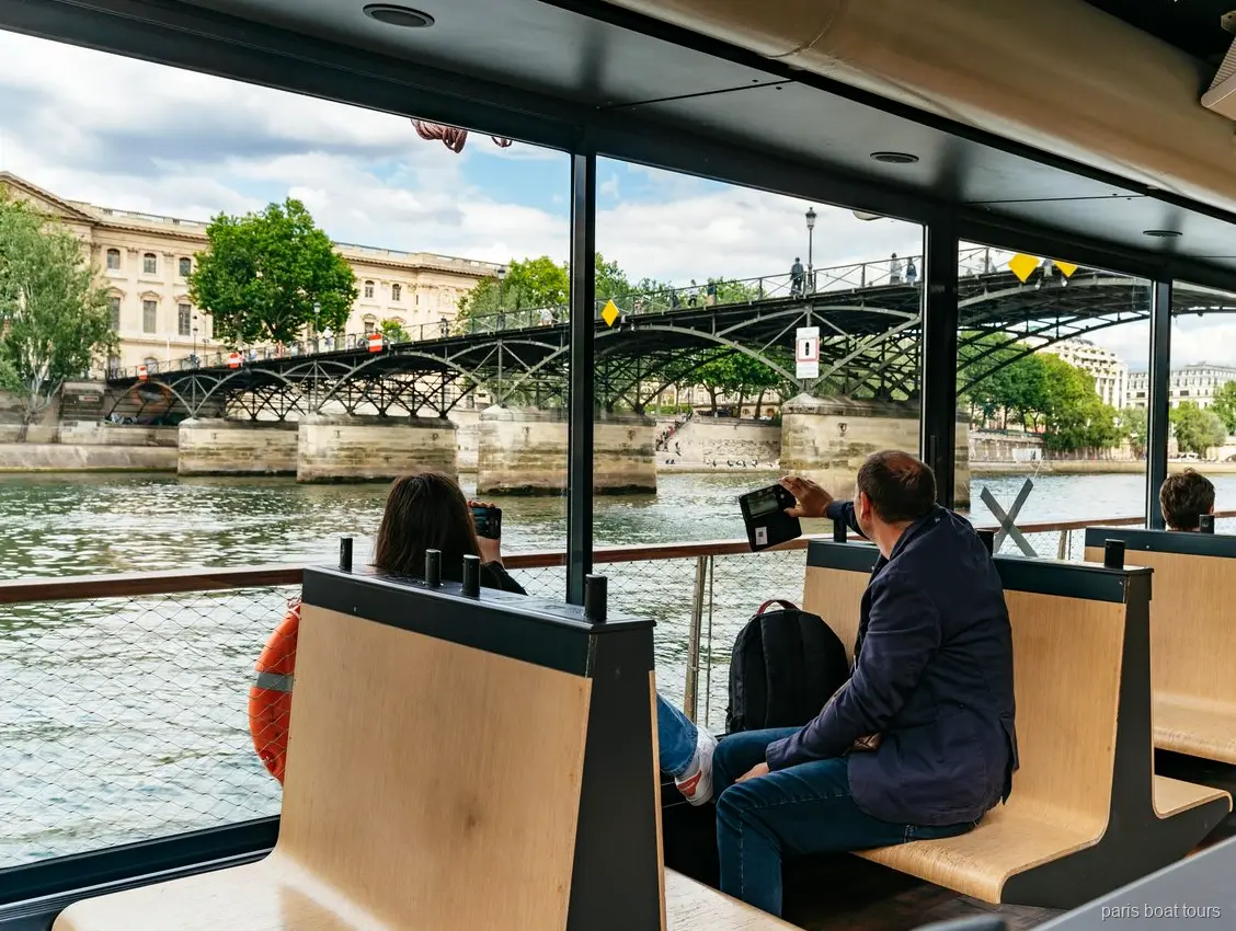Fahrgäste auf Holzbänken im Boot beobachten eine Fußgängerbrücke über der Seine, Bootstouren in Paris
