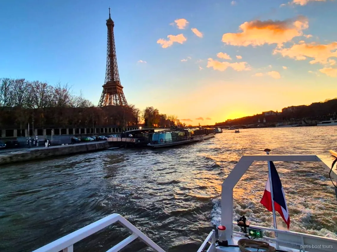 Eiffeltårnet mod en solnedgangshimmel set fra agterdækket på en sejltur i Paris med fransk flag