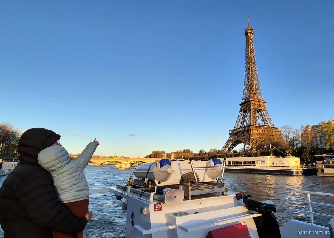 Gün batımında çocuğu kucaklayan bir yetişkin Paris tekne turunda Eyfel Kulesi'ni gösteriyor