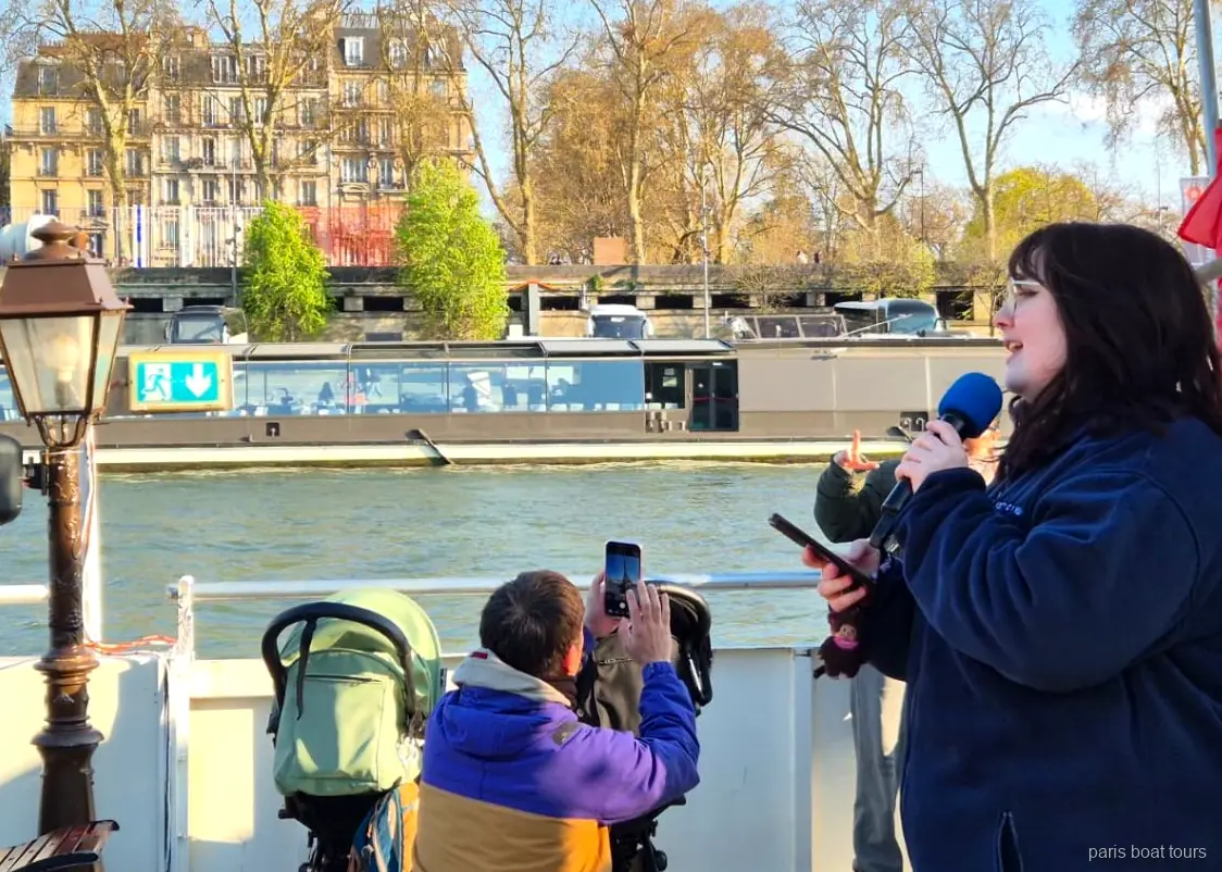 Guia parlant per un micròfon a coberta mentre els passatgers filmen el riu, passejades en vaixell per París