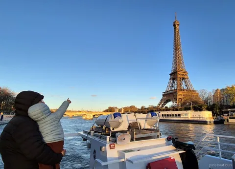 Adult amb un nen en braços que assenyala la Torre Eiffel a la posta de sol en un creuer per París