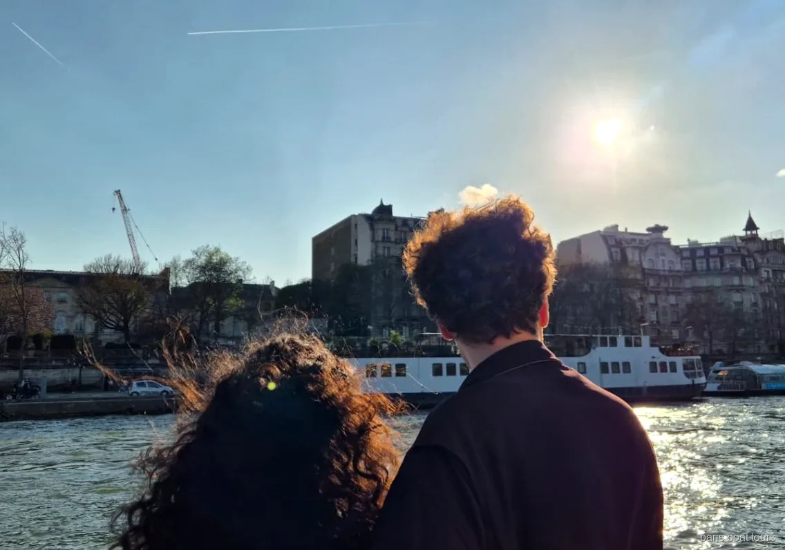 Due passeggeri guardano la Senna al sole e una barca ormeggiata dal ponte, giri in barca a Parigi