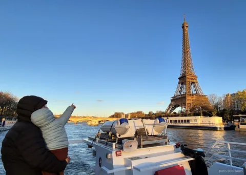 Adulto con un bambino in braccio indica la Torre Eiffel al tramonto durante un tour in barca a Parigi