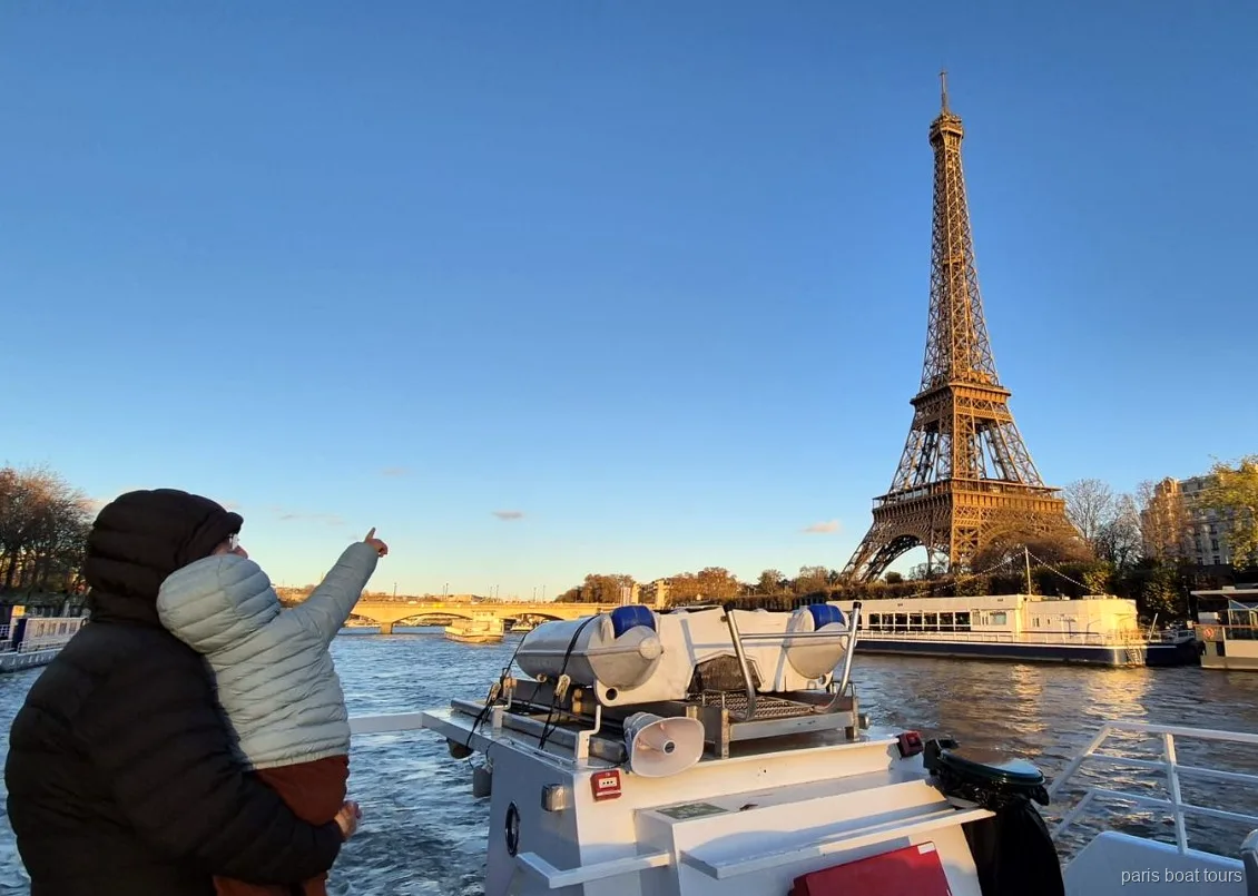 Adulto con un bambino in braccio indica la Torre Eiffel al tramonto durante un tour in barca a Parigi