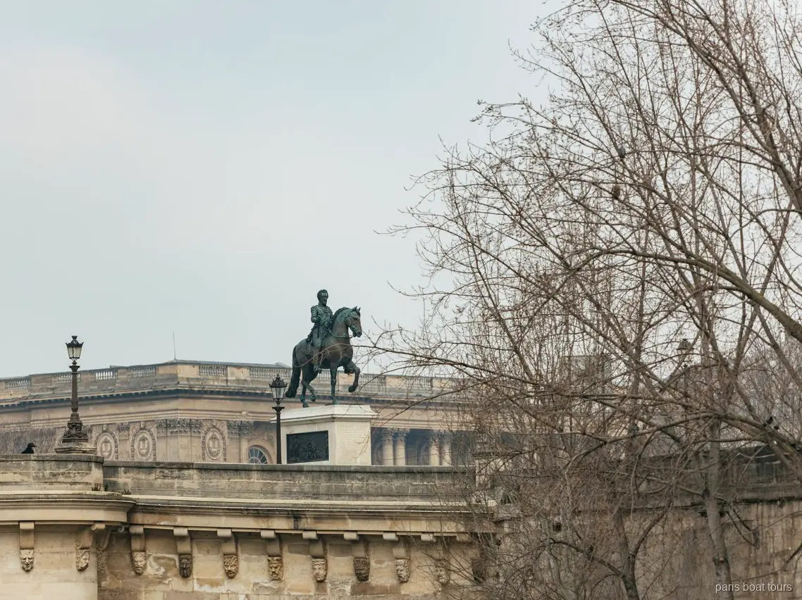 Statue équestre en bronze sur un pont de pierre derrière des arbres nus, vue en croisière à Paris