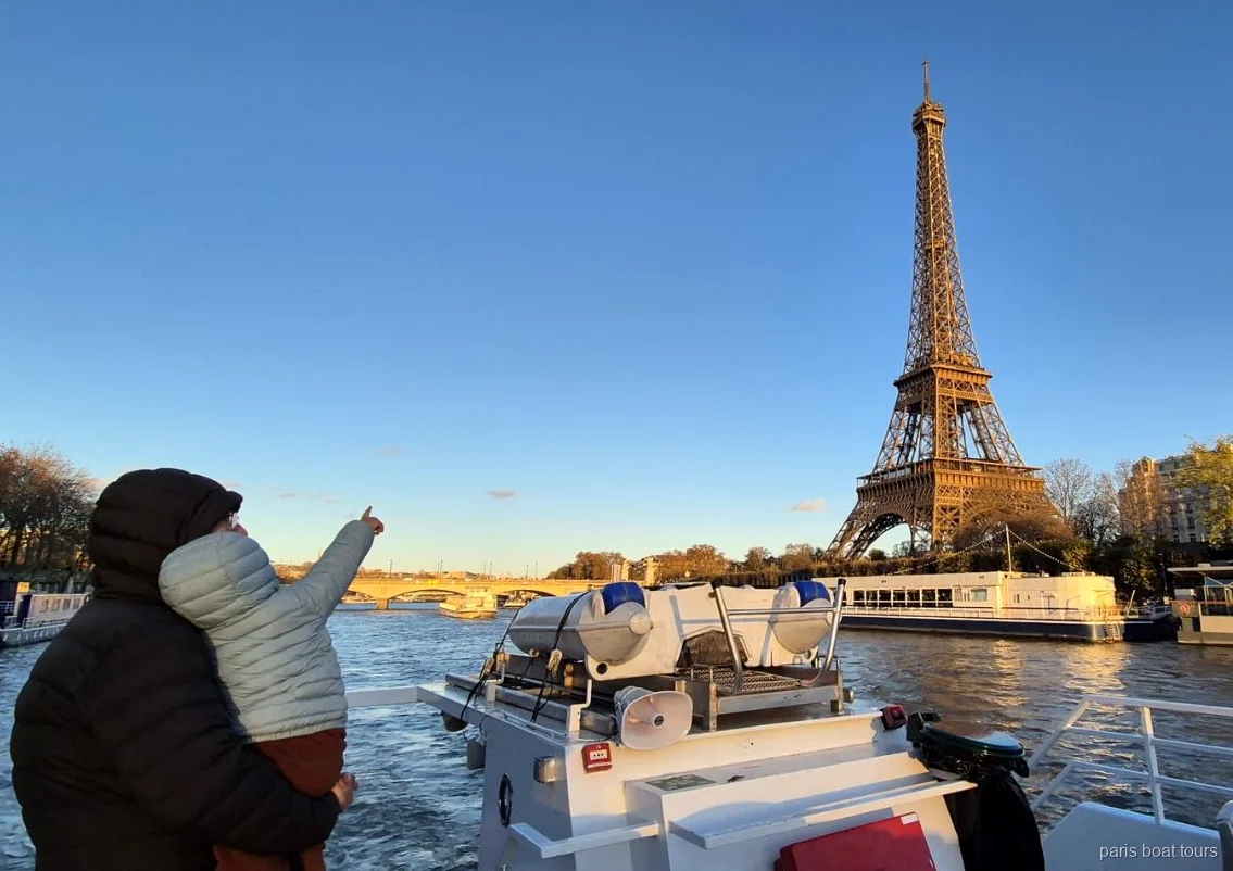 Adulte portant un enfant qui montre la tour Eiffel au coucher du soleil lors d'une croisière à Paris