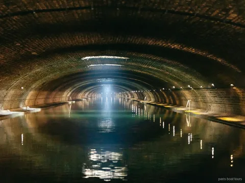 Túnel abovedado de ladrillo con un haz de luz sobre el agua en paseos en barco por París