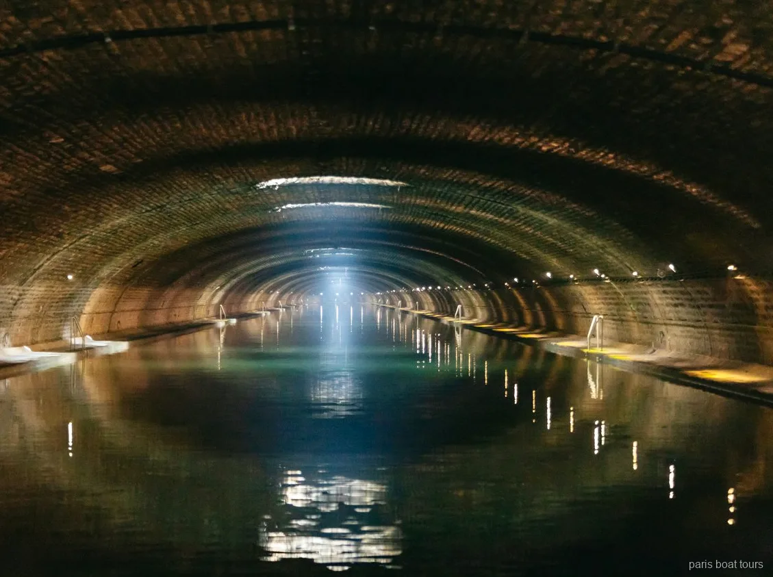 Túnel abovedado de ladrillo con un haz de luz sobre el agua en paseos en barco por París