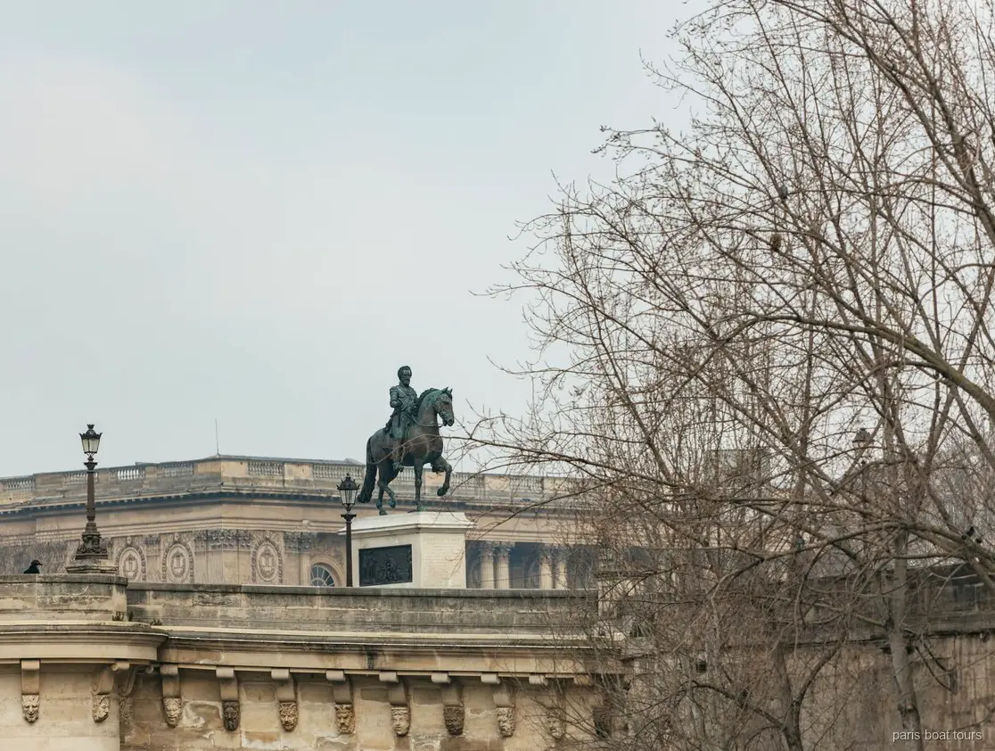 Estatua ecuestre de bronce sobre un puente de piedra tras árboles desnudos en paseos en barco por París