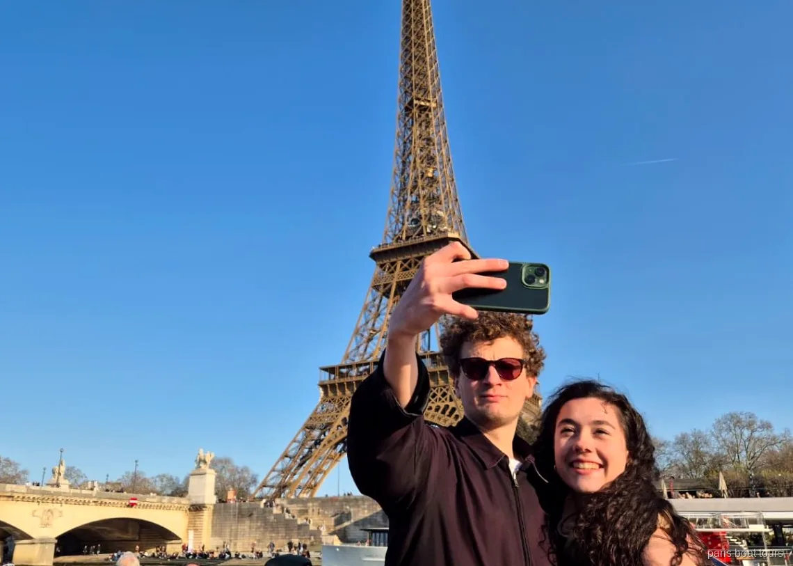 Pareja haciéndose un selfi con la Torre Eiffel detrás en uno de los paseos en barco por París