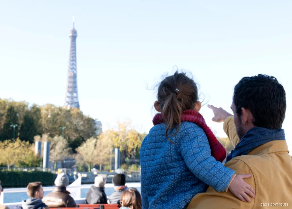 Adulto y niño señalando la Torre Eiffel desde la cubierta de uno de los paseos en barco por París