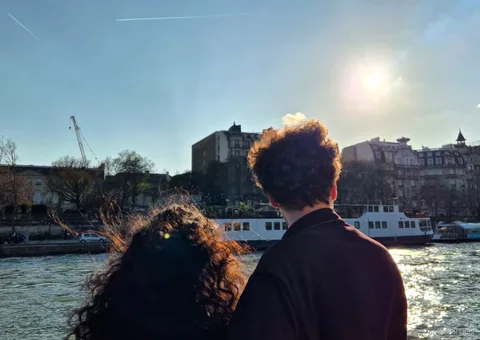 Dois passageiros olham do convés para o Sena ensolarado e um barco atracado, passeios de barco em Paris