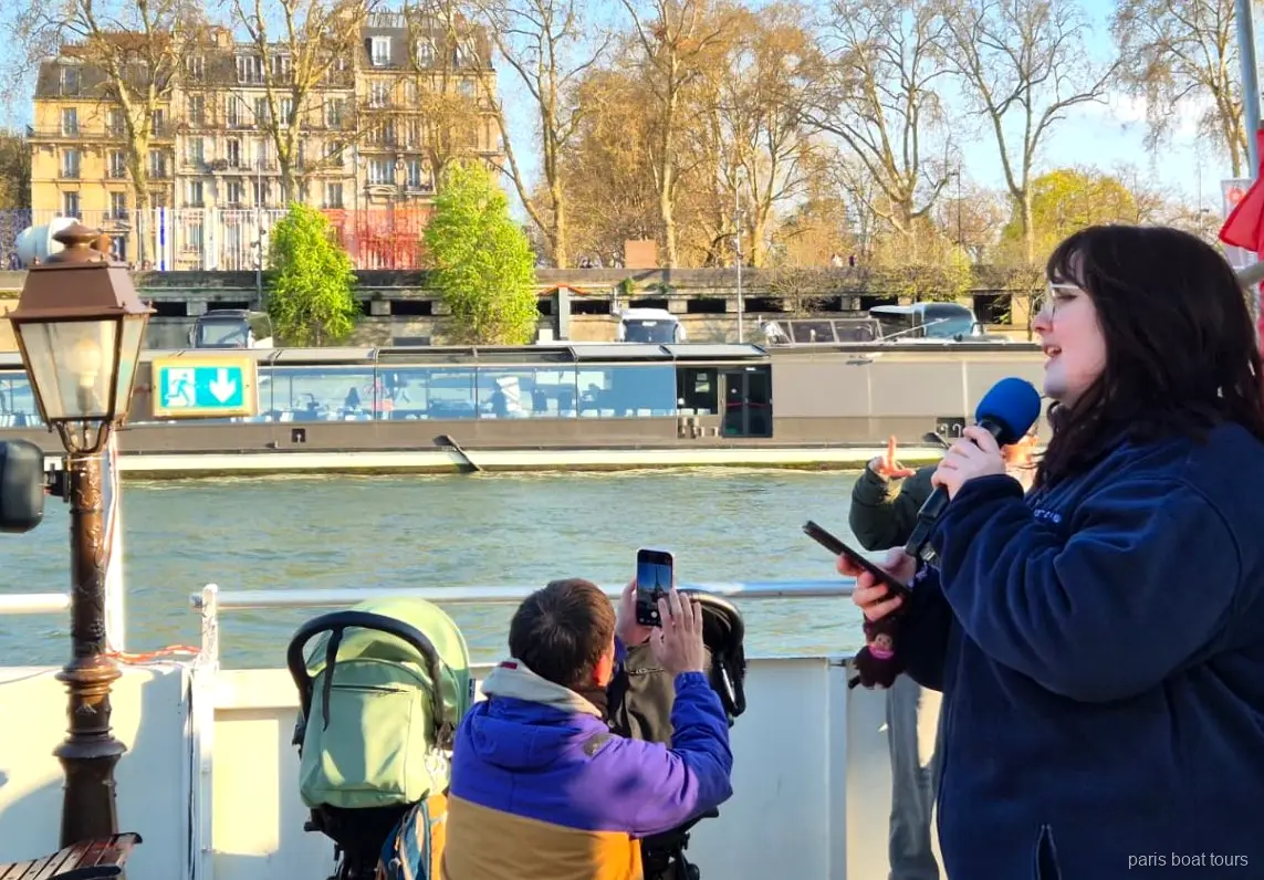 Guia falando ao microfone no convés enquanto passageiros filmam o rio, passeios de barco em Paris