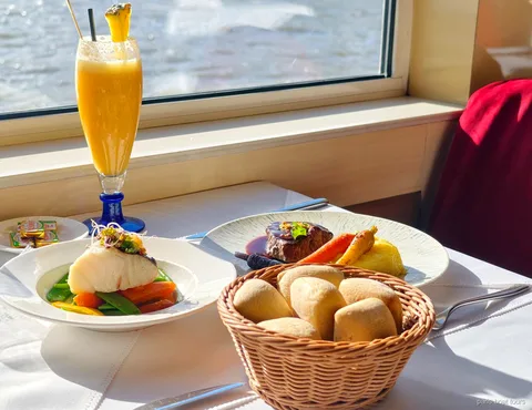 Table près de la fenêtre avec poisson, viande, corbeille de pain et jus de fruit, vue sur le fleuve, croisières à Paris