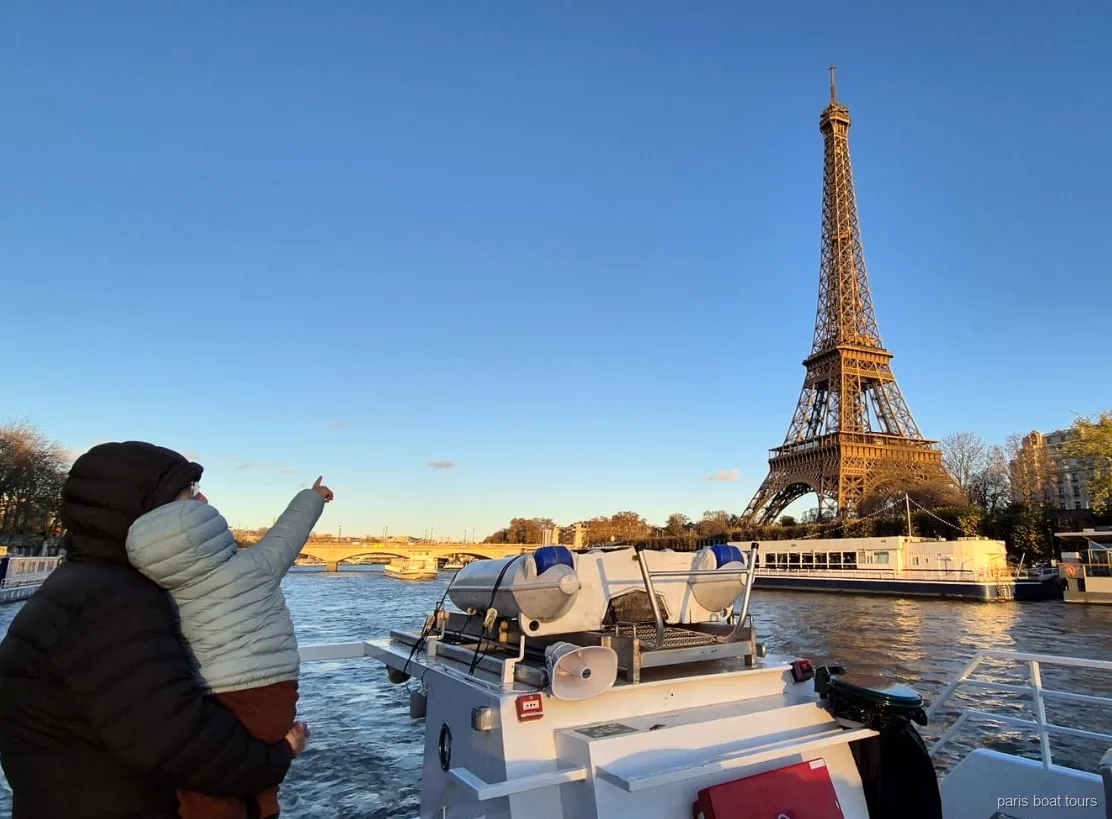 Erwachsener mit Kind zeigt bei Sonnenuntergang auf den Eiffelturm während einer Paris Bootstour auf der Seine