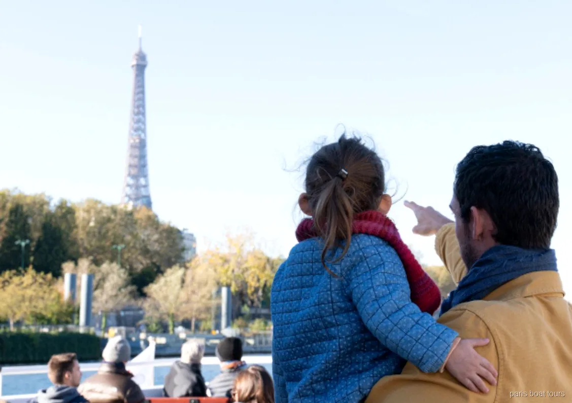 Vuxen och barn pekar på Eiffeltornet från däcket på en av båtturerna i Paris