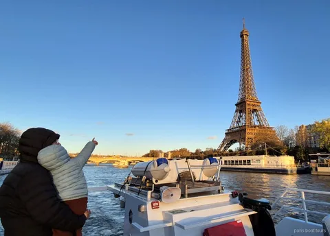Adult holding a child who points at the Eiffel Tower at sunset on Paris boat tours along the Seine