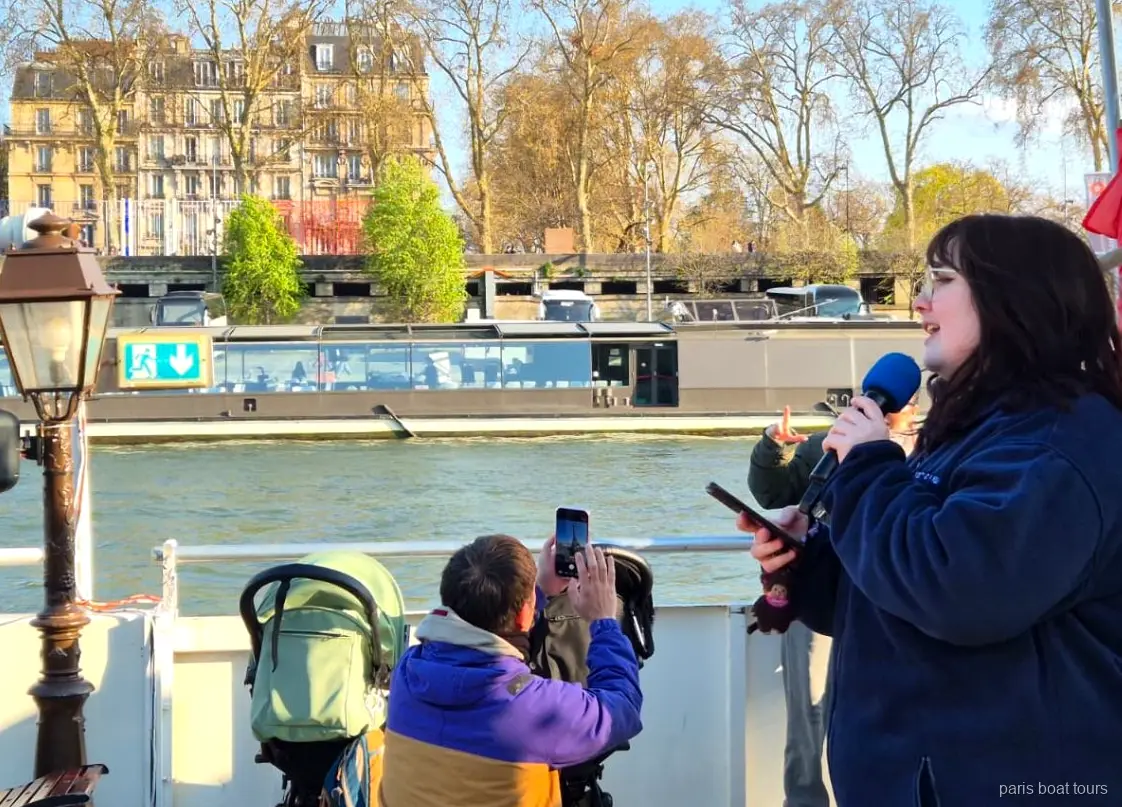 Guide speaking into a microphone on deck while passengers film the river on Paris boat tours