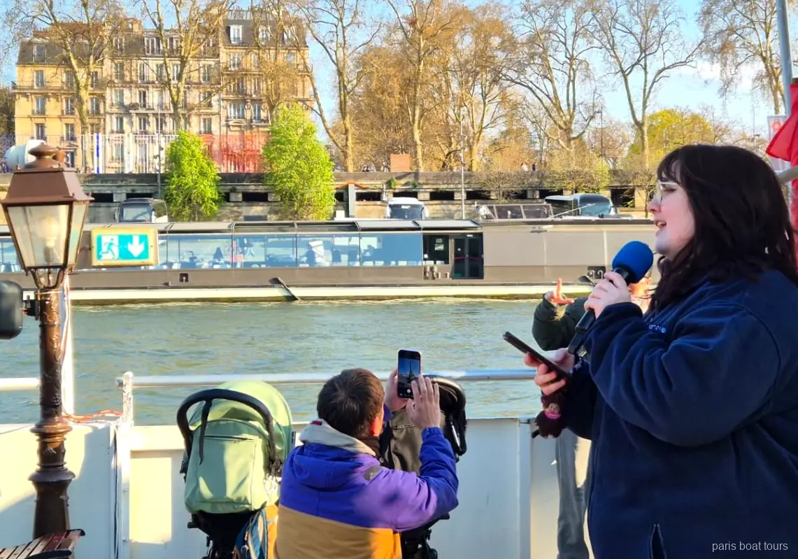 Guide taler i mikrofon på dækket, mens passagerer filmer floden på bådture i Paris