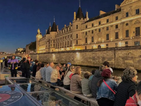 Passageiros no convés à noite diante de um edifício histórico iluminado na margem, passeios de barco em Paris