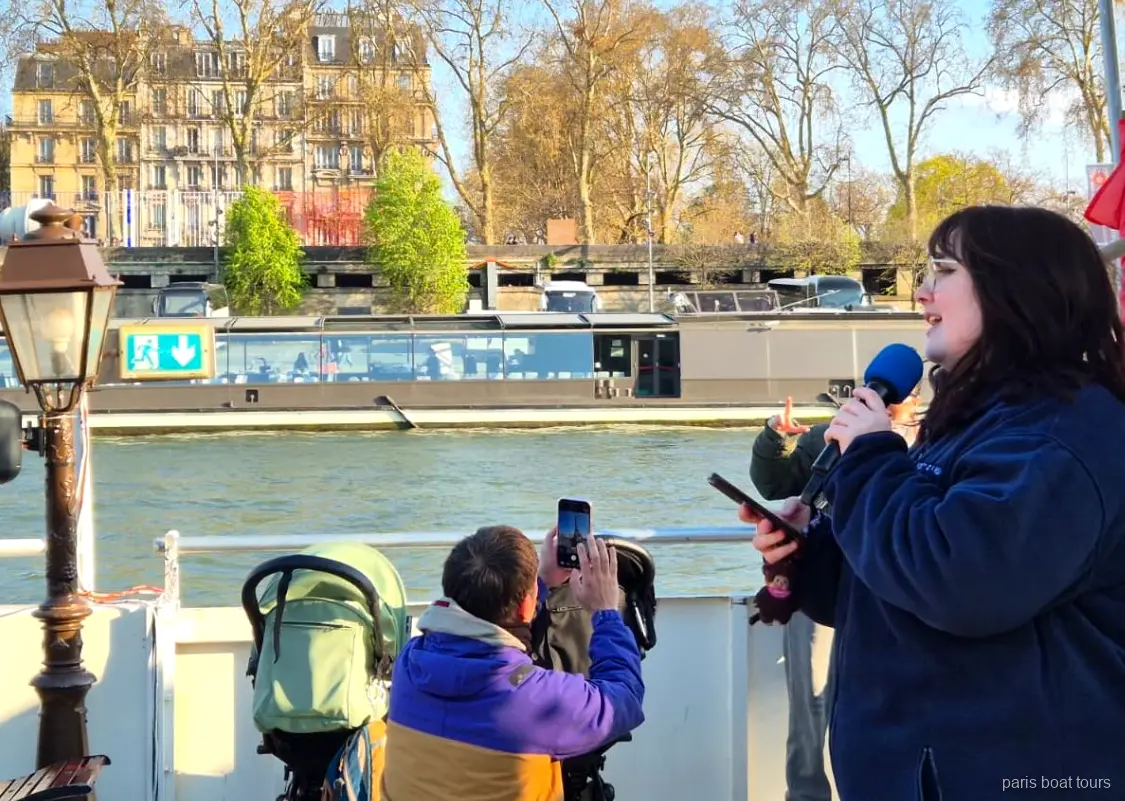 Güvertede mikrofonla konuşan rehber ve nehri çeken yolcular, Paris tekne turları