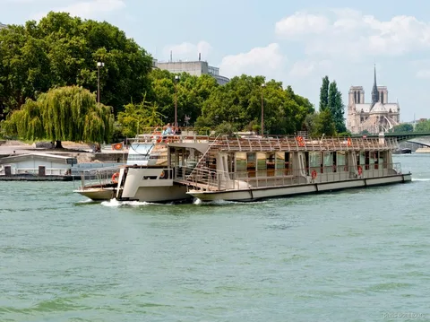 Statek z biletem Seine River Pass płynie wzdłuż zielonych brzegów, w tle Notre-Dame, rejs po Paryżu