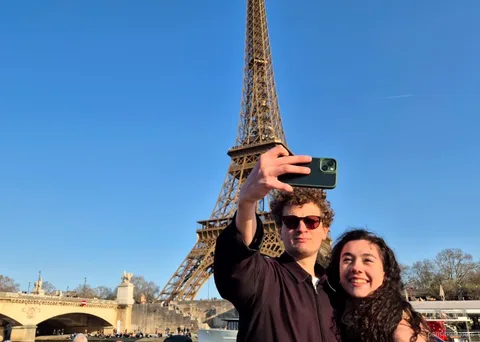 Para robi selfie na tle Wieży Eiffla podczas jednego z rejsów po Paryżu
