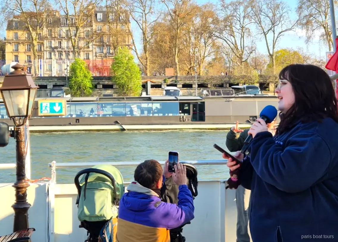 Gids spreekt in een microfoon op het dek terwijl passagiers de rivier filmen, boottochten Parijs