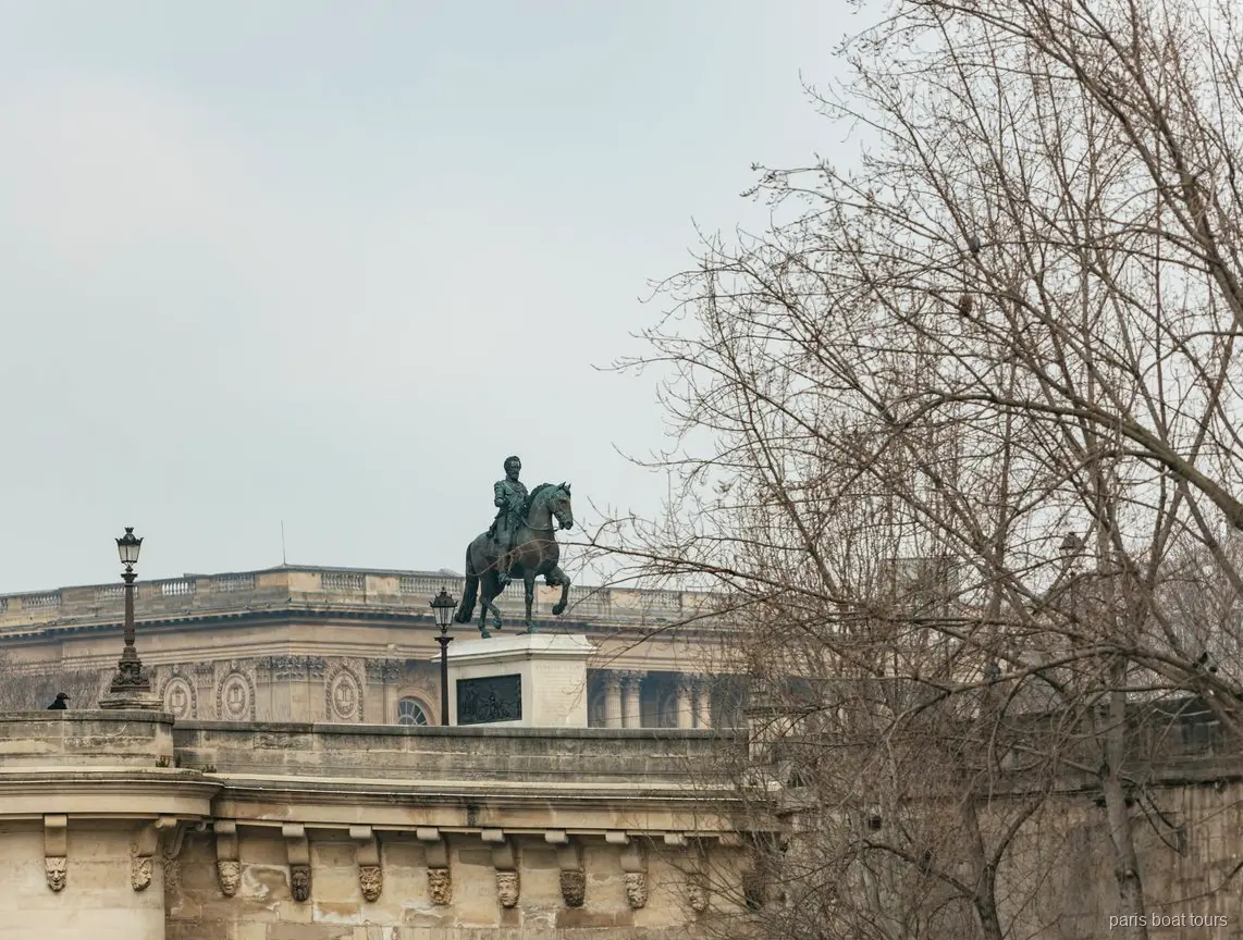 Bronze equestrian statue on a stone bridge above bare winter trees, seen on Paris boat tours