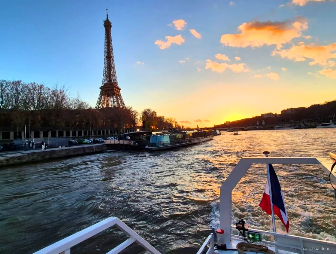 Eiffelturm vor Sonnenuntergangshimmel vom Heck einer Paris Bootstour mit französischer Flagge