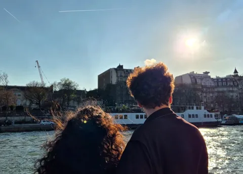 Twee passagiers van achteren kijken naar de Seine-oever en een passerend schip in laagstaande zon bij boottochten in Parijs