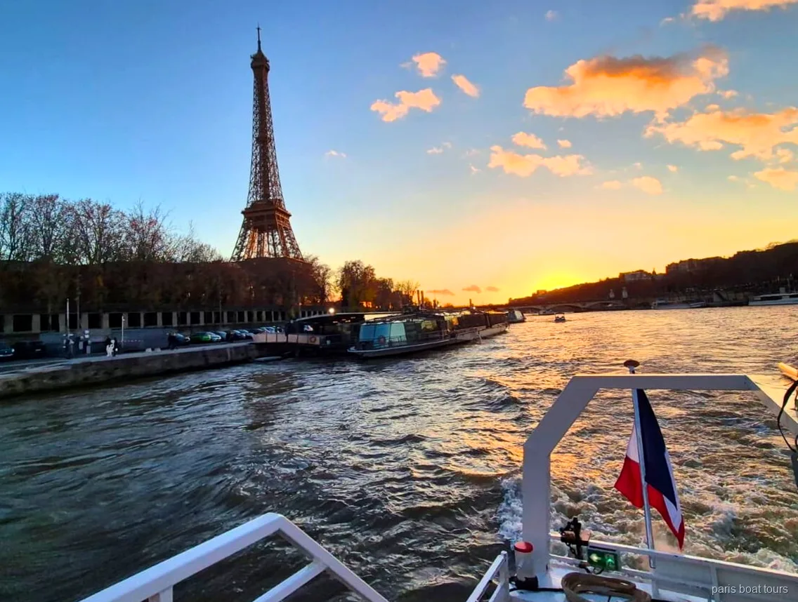 Eiffeltoren tegen een zonsonderganghemel gezien vanaf het achterdek van een boottocht in Parijs met Franse vlag