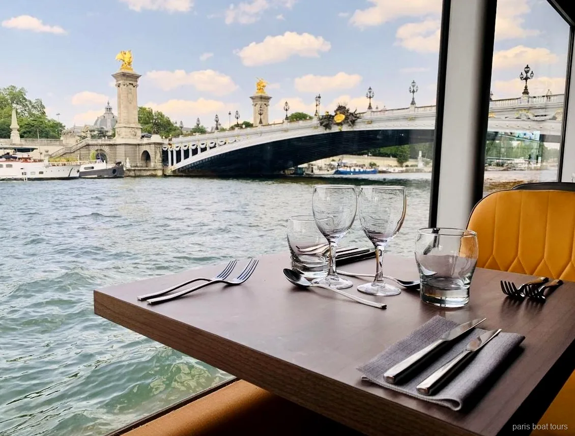 Window table set for dinner on a Paris boat tours cruise with Pont Alexandre III across the Seine