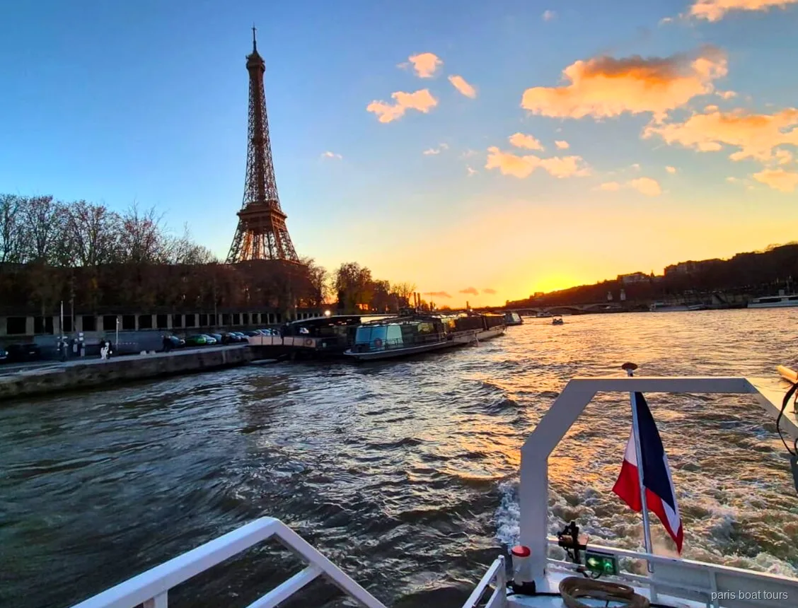 Eiffel Tower silhouetted against a sunset sky from the stern of a Paris boat tour with a French flag