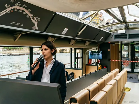 Guide with a microphone inside a glass-roofed boat beside a route map, Paris boat tours