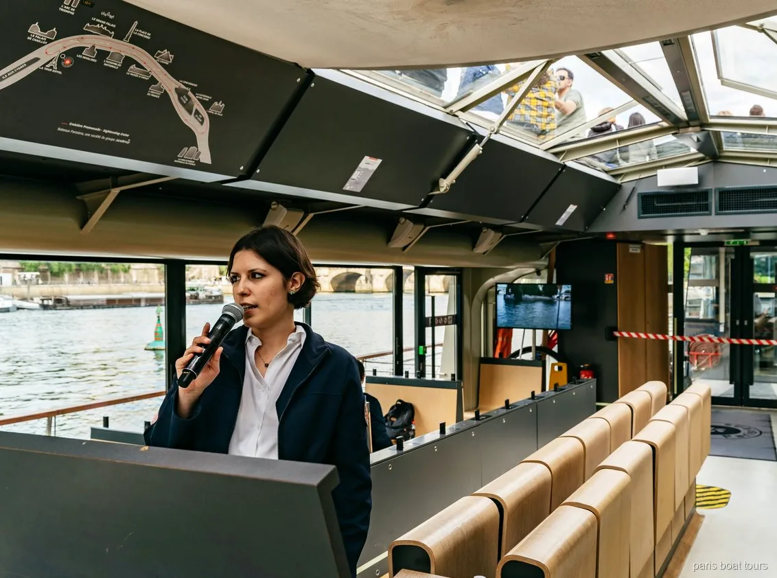 Guide with a microphone inside a glass-roofed boat beside a route map, Paris boat tours