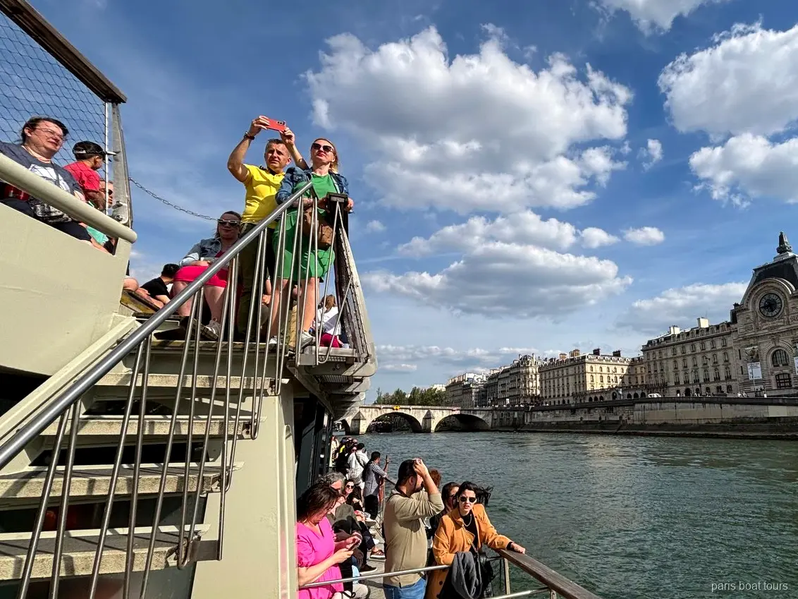 Passengers on the upper deck under a blue sky with the Musée d'Orsay on the Seine bank, Paris boat tours