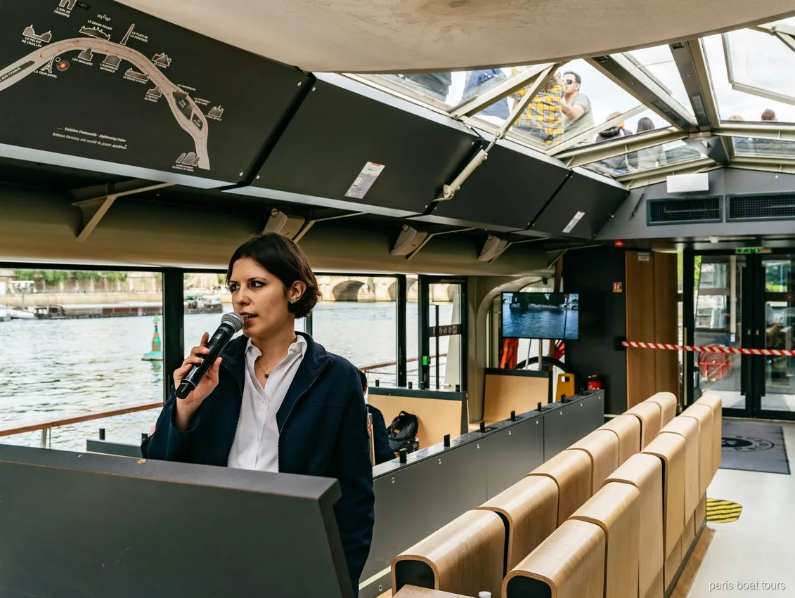 Guide med mikrofon i en båt med glastak bredvid en ruttkarta, båtturer i Paris